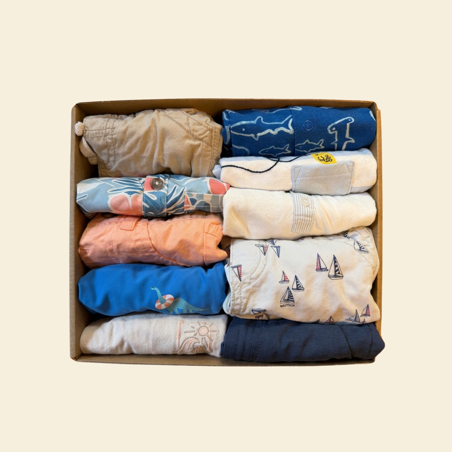 box of baby boy clothing with blue, khaki and orange color themes.