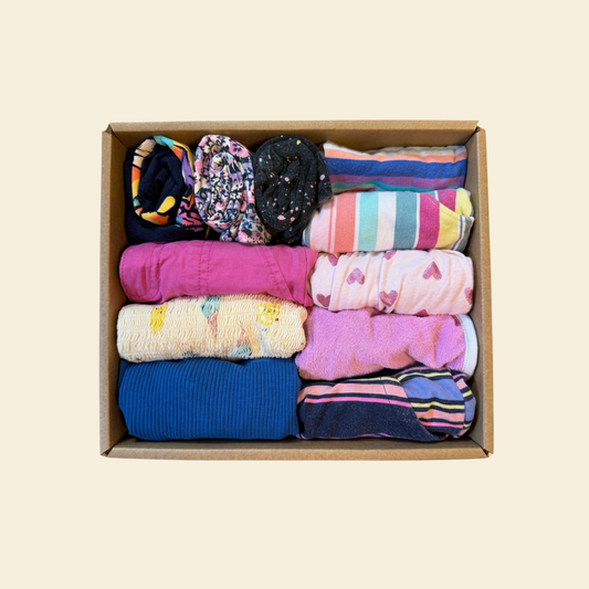 A cardboard box filled with neatly folded colorful socks or knit hosiery in various patterns and solid colors, photographed from above on a plain light beige background.