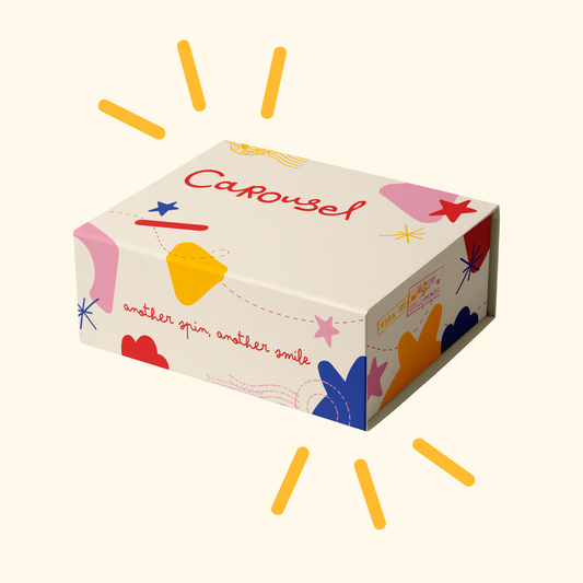 A rectangular product box with a cream background and colorful abstract shapes, including the word 'Carousel' in red script. The box is shown floating on a light cream background with yellow sunburst lines around it.